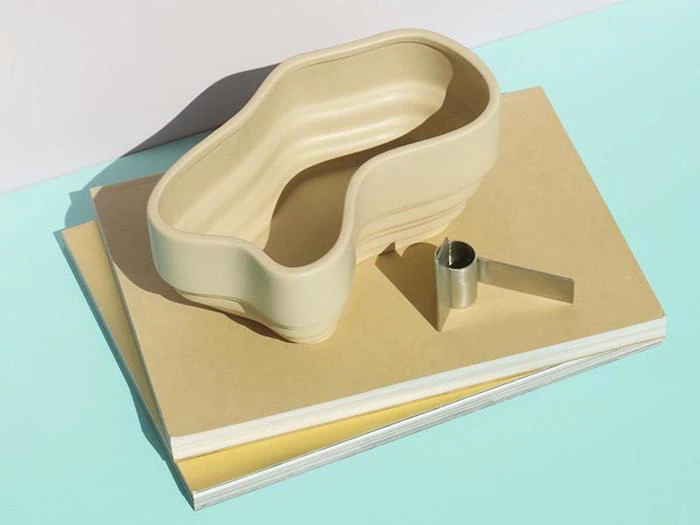 En beige, nyreformet beholder og en lille metalskovl hviler på en stak solbrune og hvide bøger på en lyseblå og hvid baggrund.