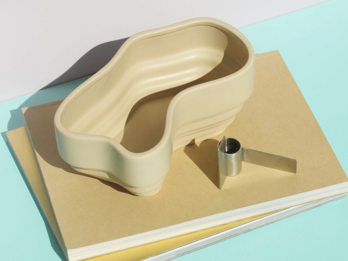 En beige nyreformet bakke og en måleske i metal ligger oven på to stablede beige notesbøger med lyseblå baggrund.