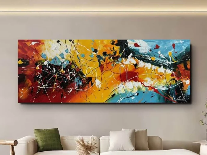 Et stort abstrakt maleri med dristige stænk af gul, rød, sort, hvid og blå hænger over en beige sofa med grønne og cremefarvede puder.