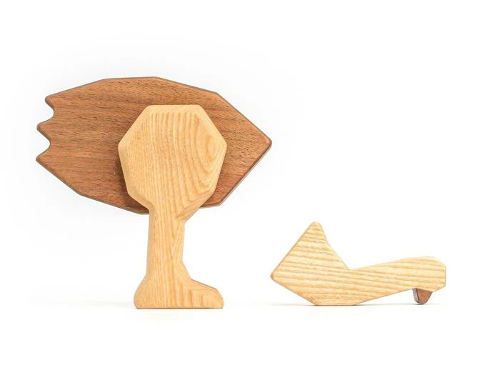 To enkle legetøjsfigurer af træ: en formet som et træ med mørkebrun top og lys stamme, og en formet som et liggende dyr, muligvis en ræv, begge på en hvid baggrund.