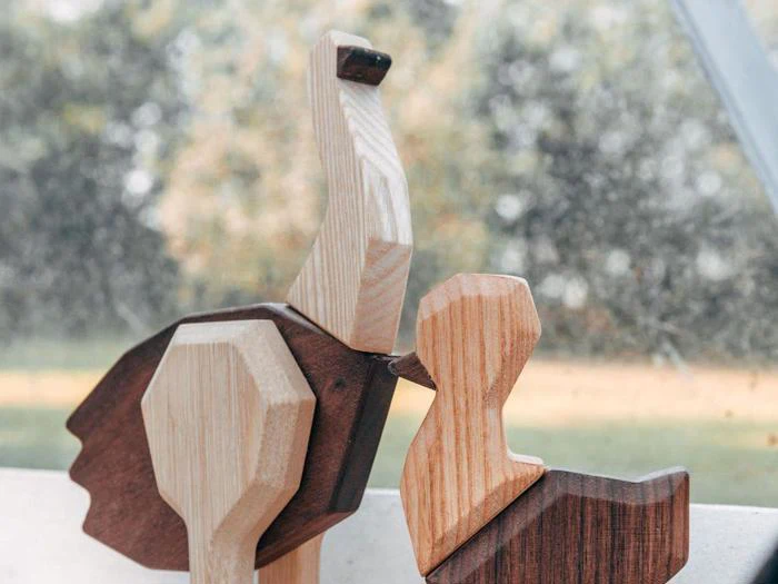 To fuglefigurer af træ, en større og en mindre, er placeret tæt sammen i en vindueskarm med en sløret udendørs baggrund.