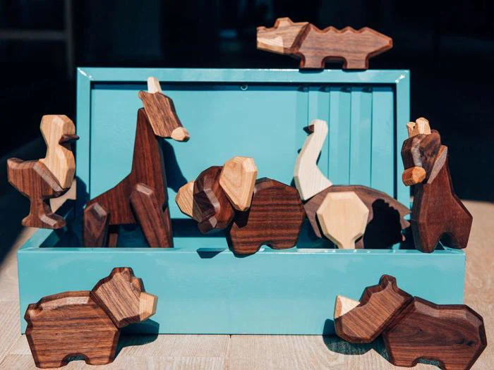 Et sæt udskårne dyrefigurer i træ, bl.a. en giraf, en elefant og en bjørn, udstillet på og omkring en blågrøn kasse på en træoverflade.