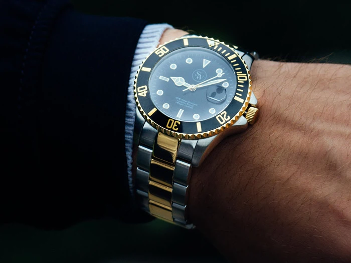 Nærbillede af et håndled iført et luksusdykkerur i sølv og guld med sort urskive og ramme, der viser klokken 10:10.