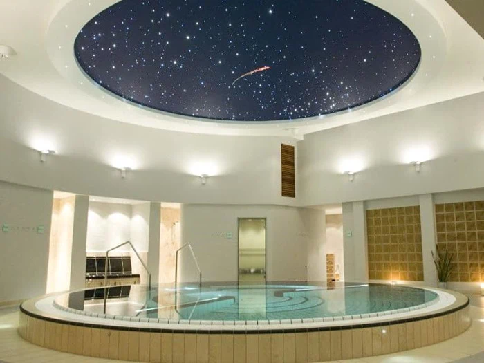 En cirkulær indendørs pool under et kuppelformet loft med en stjerneklar nattehimmel skaber en afslappende og luksuriøs atmosfære.