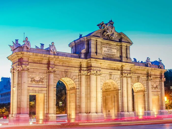 Puerta de Alcalá i Madrid, Spanien, oplyst i skumringen med en klar blå himmel og slørede lys fra den forbipasserende trafik.