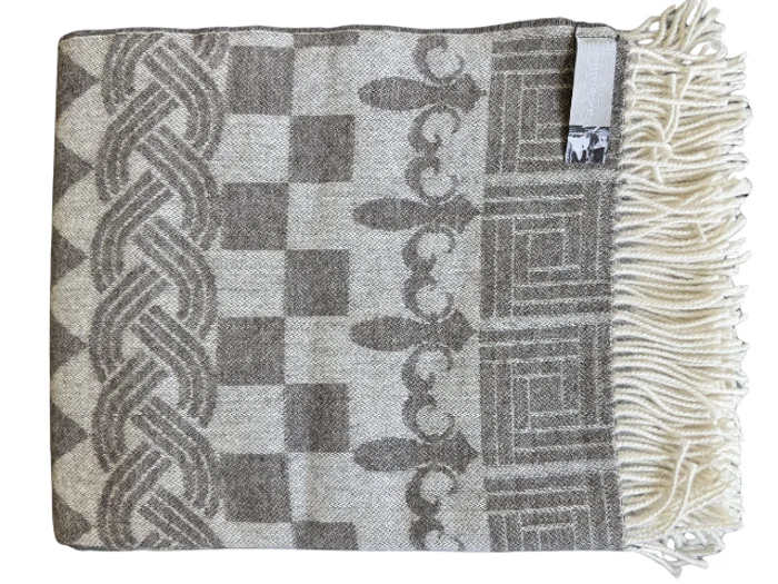 Et foldet uldtæppe med grå geometriske og udsmykkede mønstre, cremefarvede frynser på den ene kant og en lille etiket i hjørnet.
