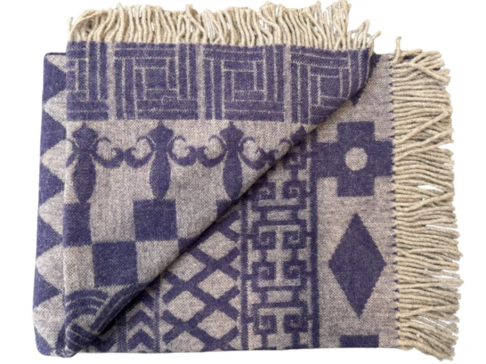 Et foldet uldtæppe med beige frynsekanter, med dristige geometriske og ornamentale lilla mønstre på en beige baggrund.