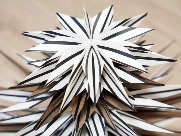 Nærbillede af en geometrisk papirstjerne med sort-, hvid- og brunstribede spidser, arrangeret i et lagdelt, pigget mønster.