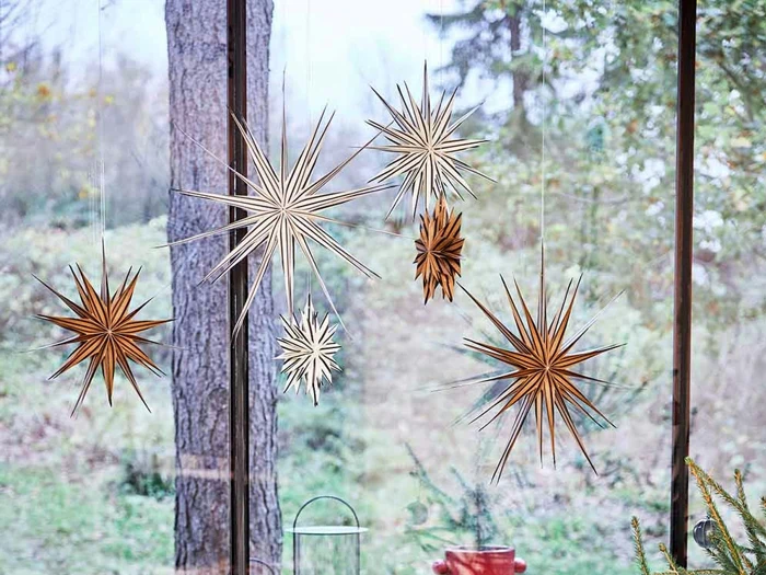 Stjernedekorationer af papir hænger foran et stort vindue med træer og grønt udenfor i baggrunden.
