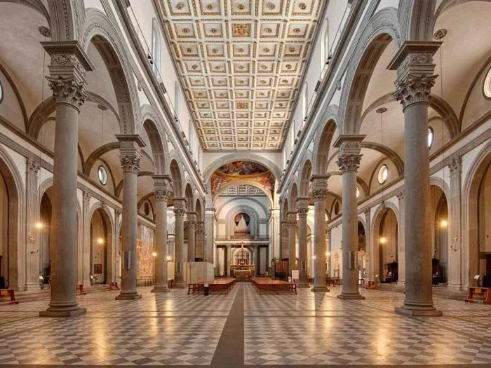 Interiør af en storslået kirke med høje søjler, buede lofter, mønstret gulv, udsmykket kassetteloft og rækker af kirkebænke, der fører til et alter i den fjerneste ende.