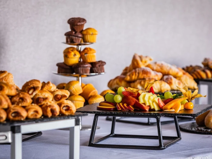 Et bord med forskelligt bagværk, muffins og et fad med frisk frugt i skiver, herunder vindruer, æbler og bær.