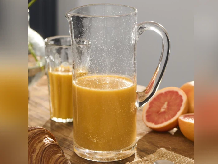 En glaskande og et glas fyldt med appelsinjuice står på et træbord ved siden af skiveskåret grapefrugt og en croissant.