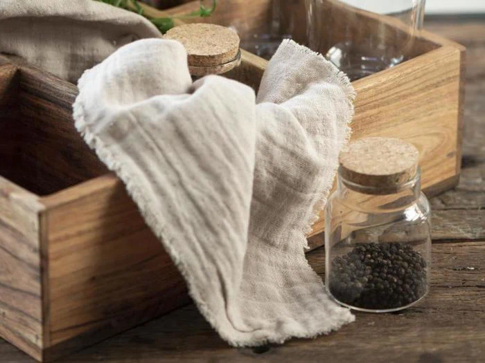 Et lysbeige klæde draperet over en trækasse står ved siden af en lille glaskrukke fyldt med sorte peberkorn på en rustik træoverflade.