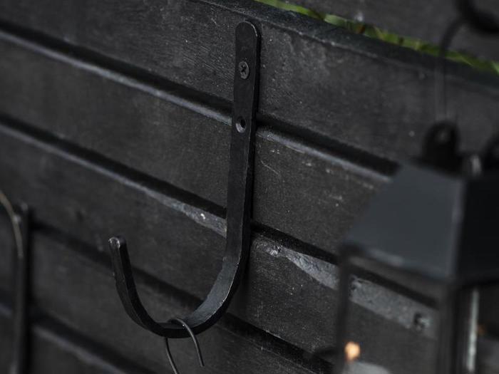 En sort metalkrog er monteret på en mørk lamelvæg af træ, og et andet objekt er delvist synligt i højre side af billedet.