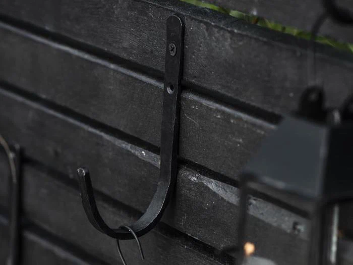 En sort metalkrog er monteret på en mørk lamelvæg af træ, og et andet objekt er delvist synligt i højre side af billedet.