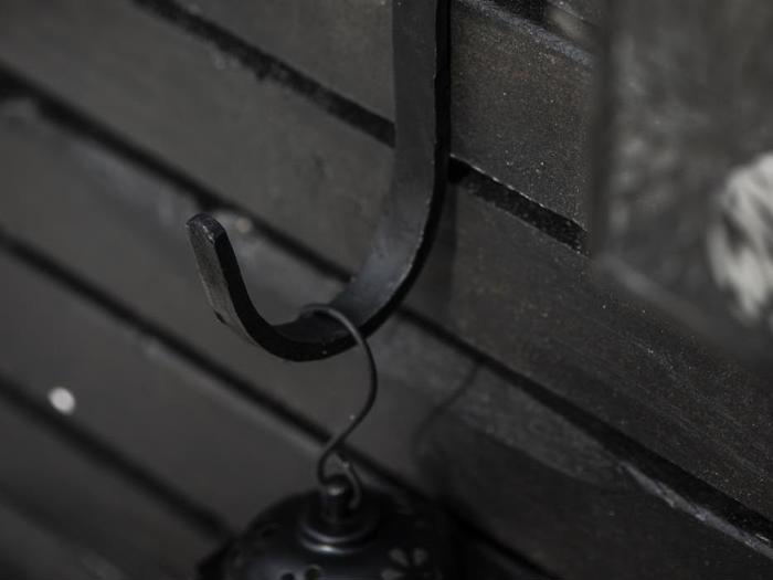 En sort metalkrog fastgjort til en mørk trævæg med en lille hængende lanterne.