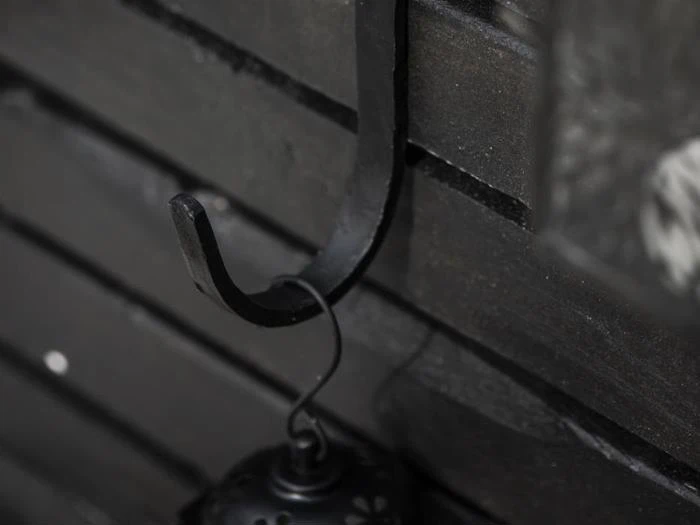 En sort metalkrog fastgjort til en mørk trævæg med en lille hængende lanterne.