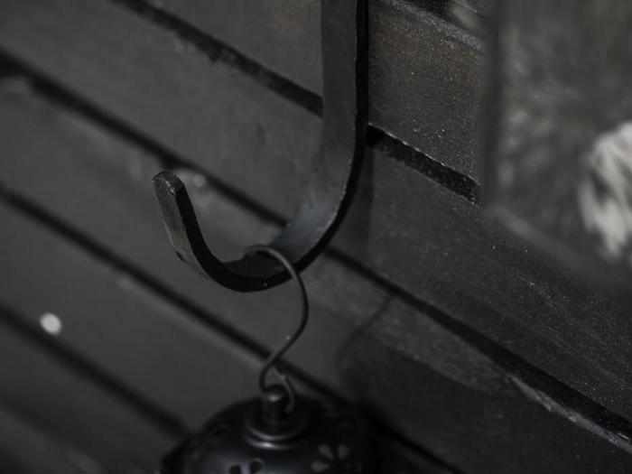 En sort metalkrog fastgjort til en mørk trævæg, der holder en lille lanterne i den øverste løkke.