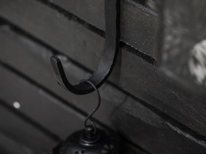 En sort metalkrog fastgjort til en mørk trævæg, der holder en lille lanterne i den øverste løkke.