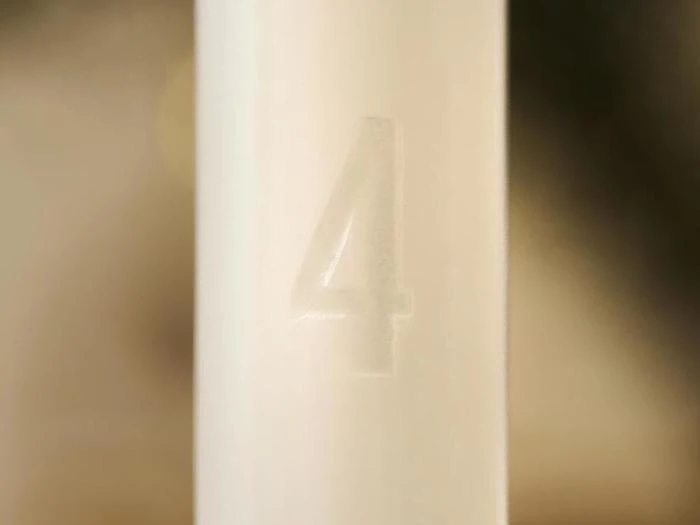 Nærbillede af et hvidt stearinlys med tallet 4 præget på overfladen.