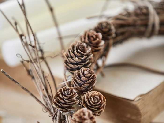 Et nærbillede af en håndlavet krans dekoreret med kogler og kviste, der hviler på en stak bøger.