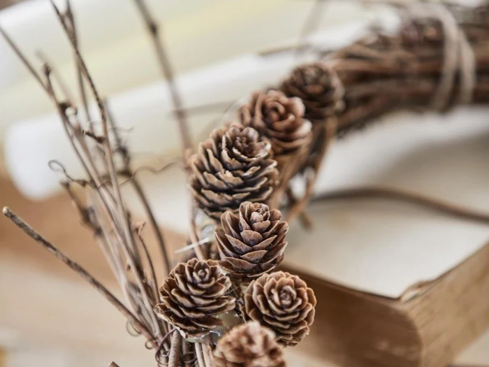 Et nærbillede af en håndlavet krans dekoreret med kogler og kviste, der hviler på en stak bøger.