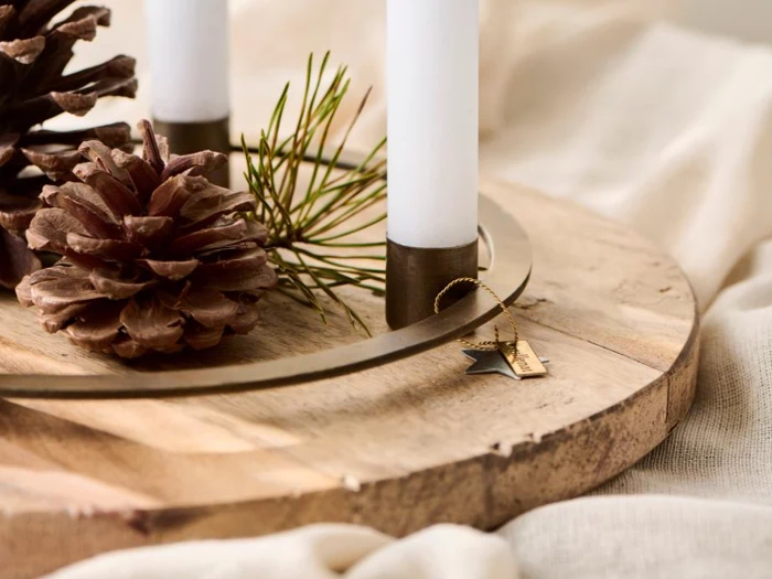 En træbakke med to hvide lys, kogler, en fyrrekvist og en lille stjerneformet dekoration skaber et hyggeligt, rustikt arrangement.