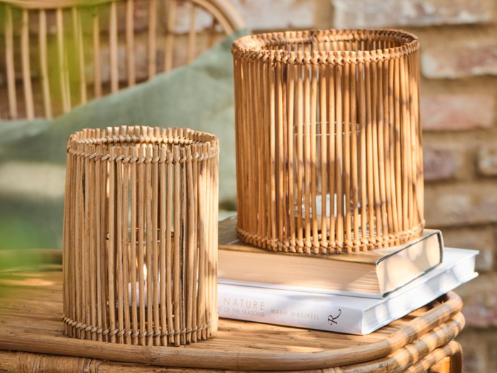 To bambuslysestager står på et kurvebord ved siden af stablede bøger med en grøn pude og en murstensvæg i baggrunden.