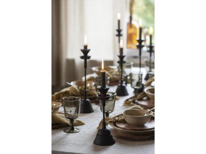 Et spisebord med tallerkener, skåle, glas og flere tændte sorte lysestager, som skaber en varm og hyggelig atmosfære.