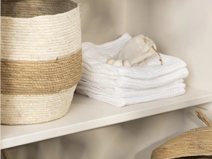 På en hvid hylde står en flettet kurv og en stak hvide håndklæder med en lille pose med løbegang og sæbebolde.