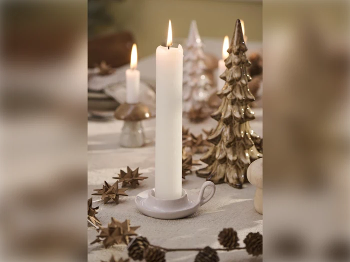 Et hvidt lys brænder i en lille holder på et pyntet bord med metallisk juletræspynt og kogler omkring.