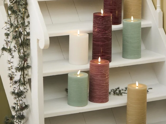 Store bloklys i grøn, rød, creme og elfenben står tændt på hvide trappetrin, og langs gelænderet er der draperet en grøn guirlande.