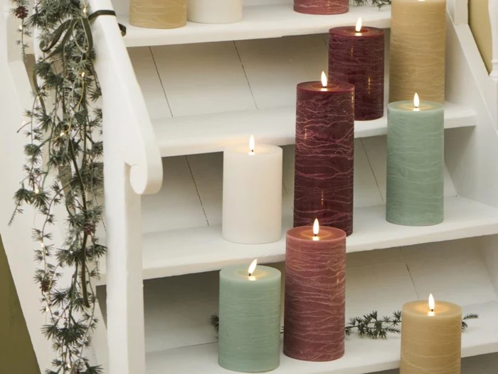 Stagelys i forskellige farver er tændt og arrangeret på hvide trapper med grønne planter, der pynter på gelænderet.