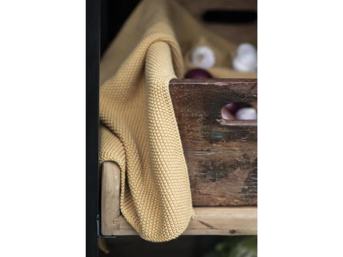 Et gult klæde med struktur er draperet over kanten af en rustik trækasse med et par synlige løg indeni.