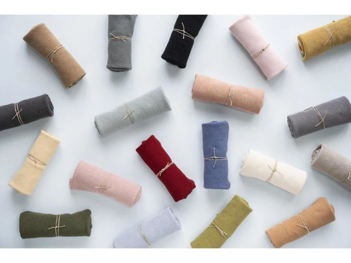 Flere sammenrullede, strukturerede stofstykker i forskellige farver er arrangeret på en lys overflade, hver bundet med en snor.