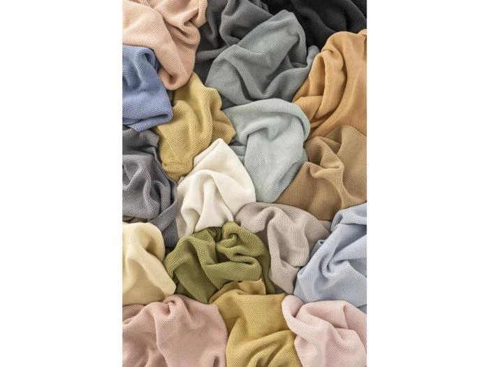 En bunke af forskellige teksturerede stofstykker i dæmpede farver som beige, grå, blå, grøn og creme, alt sammen løst samlet.