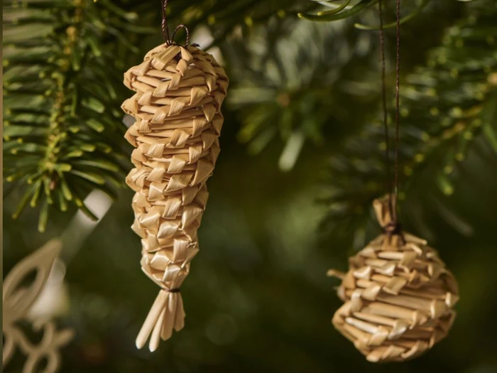 To halmjulekugler, den ene formet som en kogle og den anden som en kugle, hænger på en grøn juletræsgren.