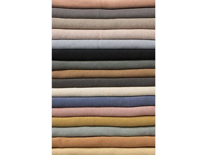 Pænt stablede lag af stof i forskellige ensfarvede farver, arrangeret vandret i et vekslende mønster af neutrale, pastelfarvede og jordfarvede toner.