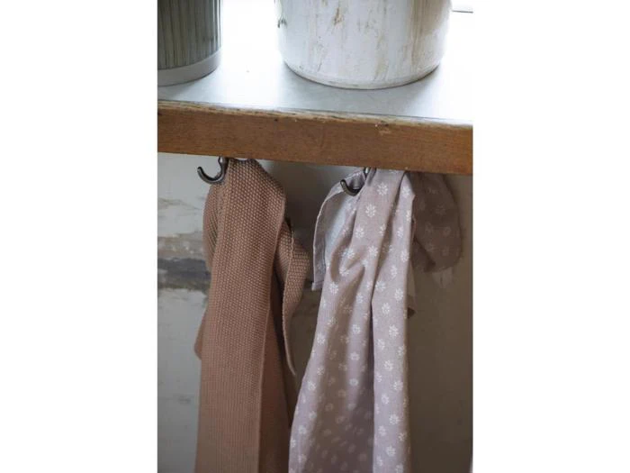 To håndklæder, et brunt og et lyst med hvidt blomstermønster, hænger på kroge under en bordplade af træ. En hvid beholder står oven på køkkenbordet.