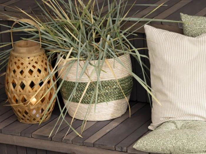 En flettet lanterne, en potteplante i en stribet kurv og to cremefarvede puder hviler på mørke trætrin.