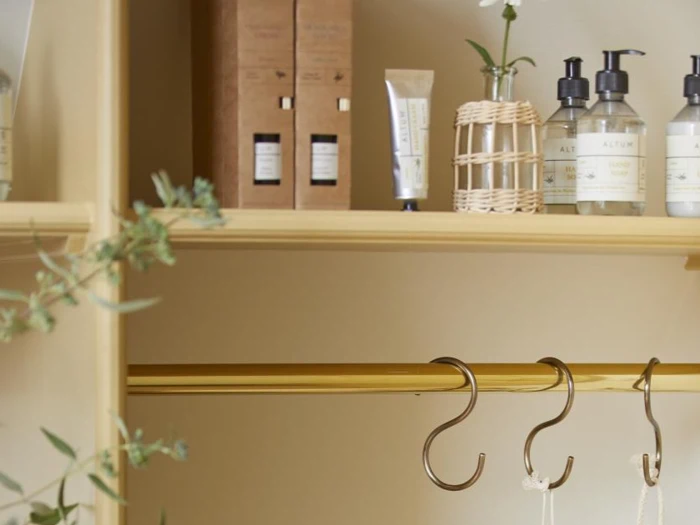 Træhylde med toiletsager, lotionflasker, en lille vase med en blomst og en tom garderobestang nedenunder med to kroge.