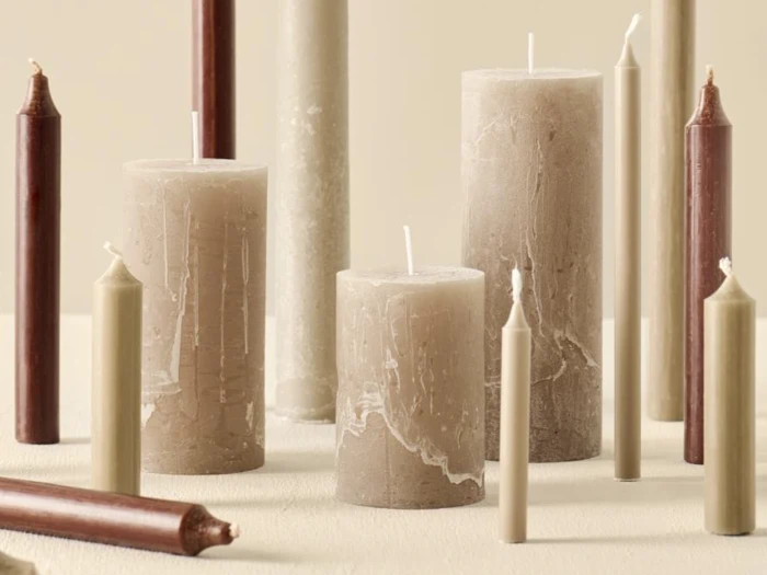 Forskellige søjle- og koniske stearinlys i beige, taupe og burgunder er anbragt både stående og liggende på en neutral baggrund.