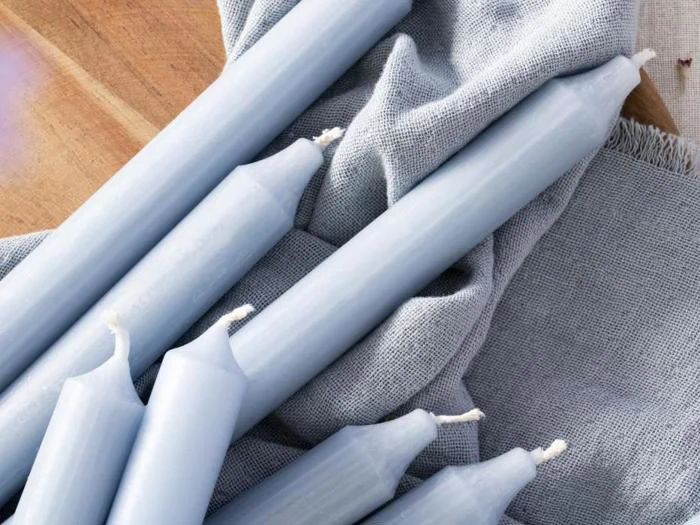 Flere lyseblå stearinlys er arrangeret oven på et lysegråt, struktureret klæde, der er placeret på en træoverflade.