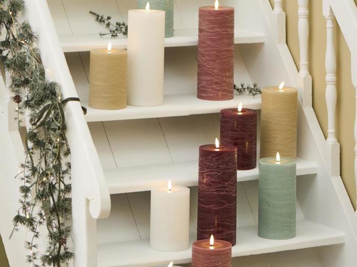 Store, tændte bloklys i forskellige farver er anbragt på en hvid trappe dekoreret med en grøn guirlande.