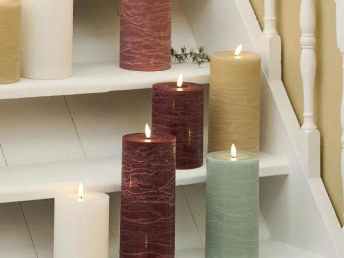 Flere tændte bloklys i forskellige farver er anbragt på en hvid trætrappe ved siden af et hvidt gelænder.