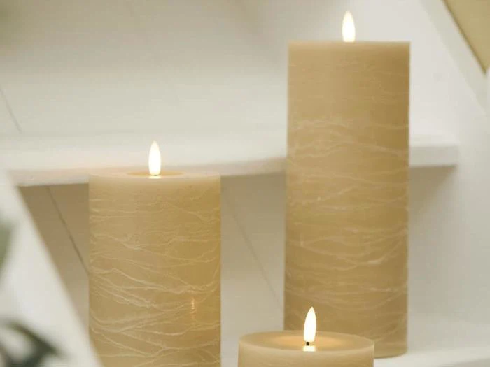 Tre beige søjlelys i forskellige højder er tændt og placeret på hvide trin, hvilket skaber en varm og beroligende atmosfære.