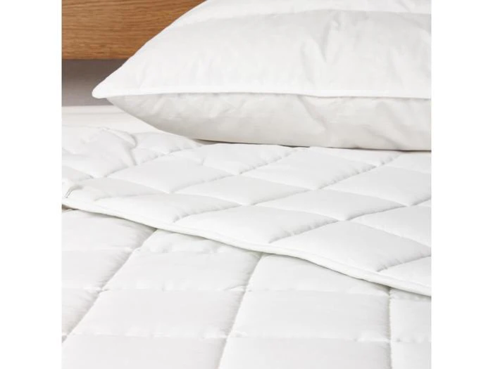 Et nærbillede af en hvid quiltet dyne på en seng med en matchende hvid pude i baggrunden.