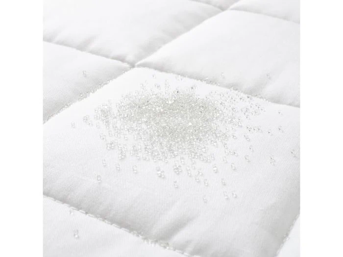 Klare perler eller små krystaller spredt på en hvid, quiltet stofoverflade, muligvis en del af en madras eller sengetøj.