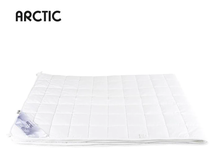 Et hvidt quiltet tæppe er pænt foldet på en hvid baggrund med et mærke i det ene hjørne. Ordet ARCTIC står i sort tekst øverst til venstre.