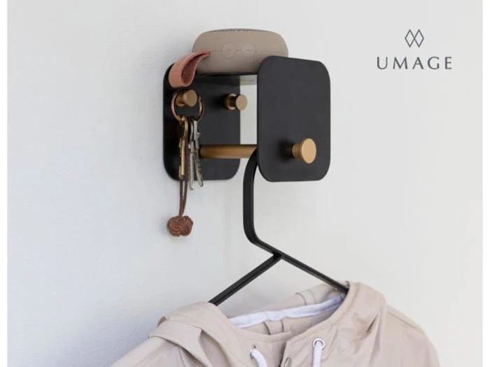 En moderne væghængt organizer i sort og guld rummer nøgler, en smarthøjttaler og en jakke på en bøjle med UMAGE-logoet synligt på væggen.